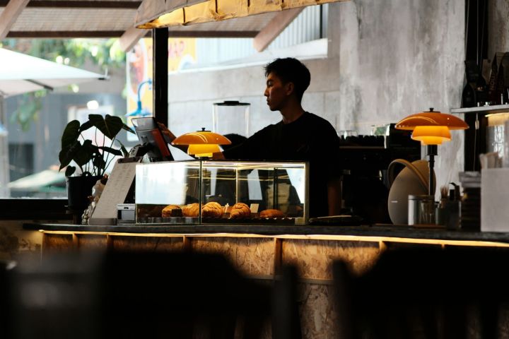 Cafe owner behind counter Cafe owner working alone behind the counter under warm pendant lamps