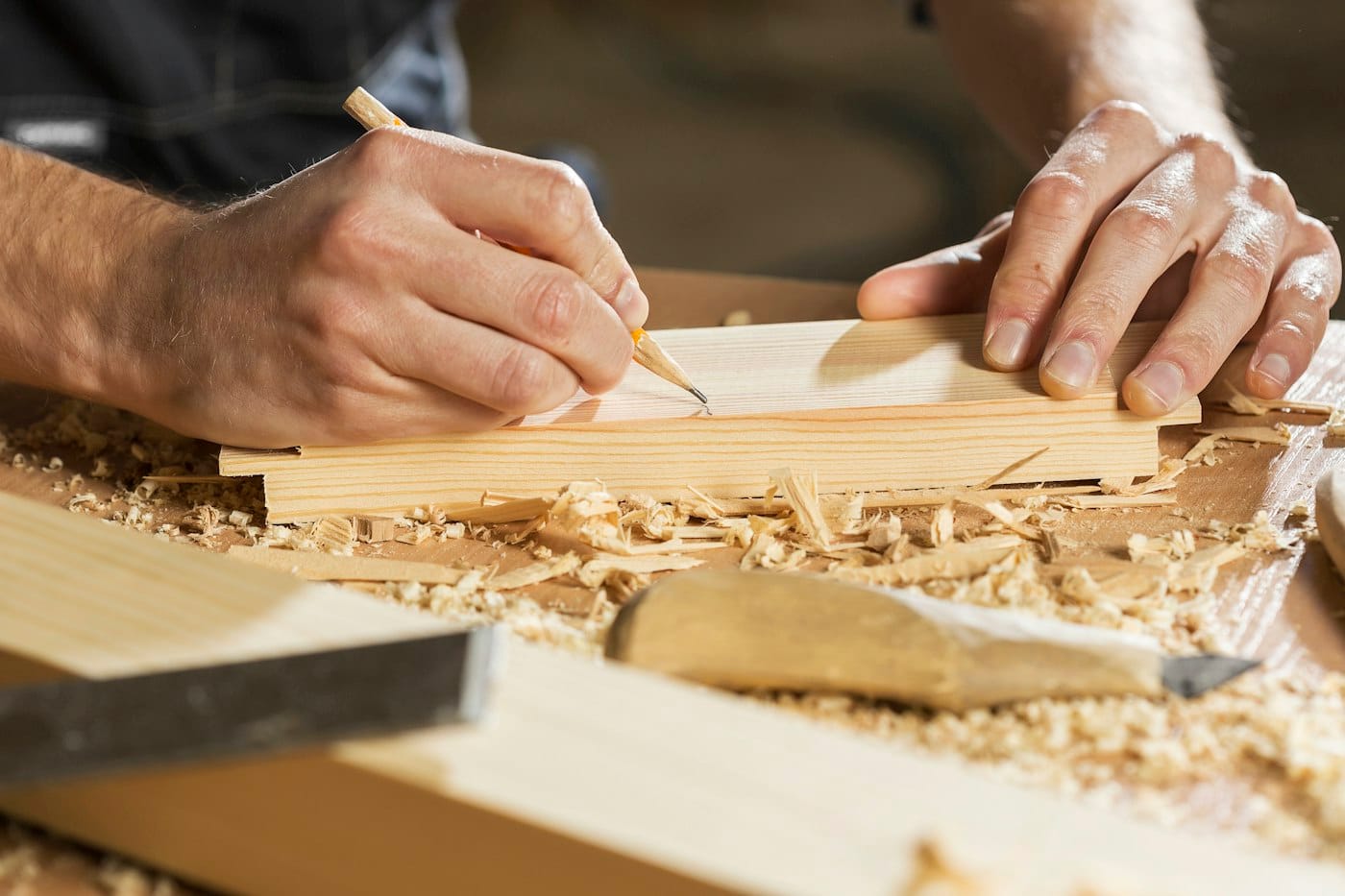 Carpenter's hand marking a length of timber with a pencil