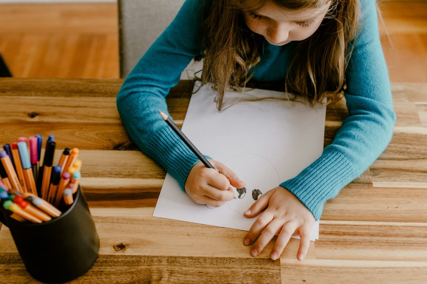 Child drawing at a timber kitchen table with coloured pencils