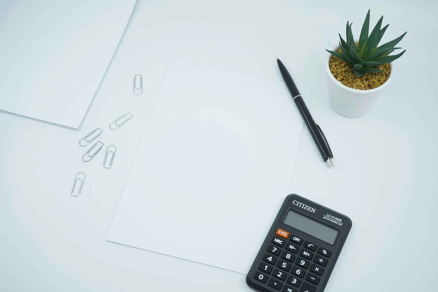 Tidy white desk with a calculator, pen and paper