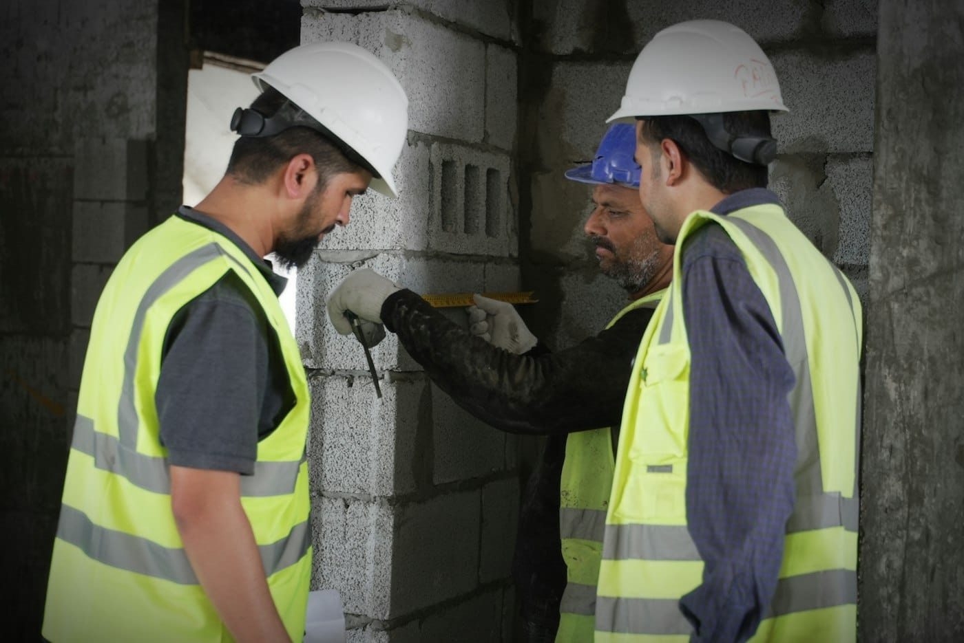 Workers in hi-vis vests and hard hats measuring a blockwork wall