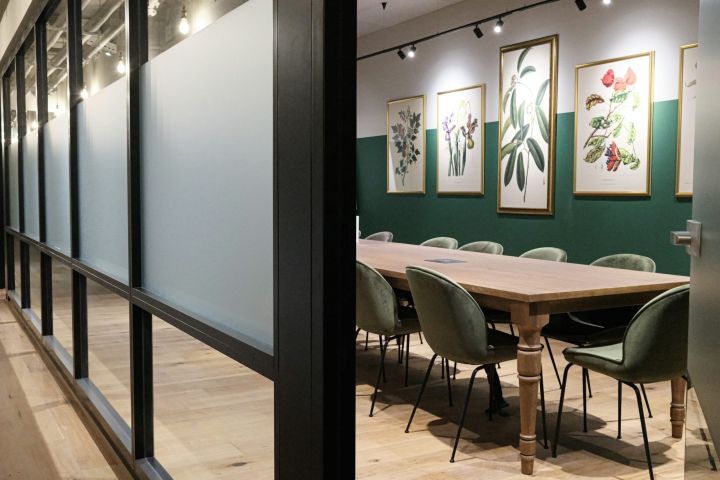 Quiet meeting room with a long timber table, velvet chairs and botanical prints on a deep green wall