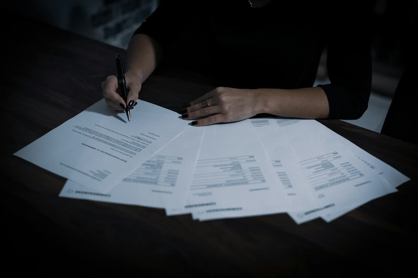 Woman signing loan documents at a table spread with paperwork
