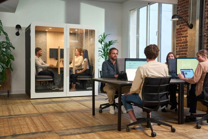 Team shared office Team working at shared desks in a bright office with plants and brick walls