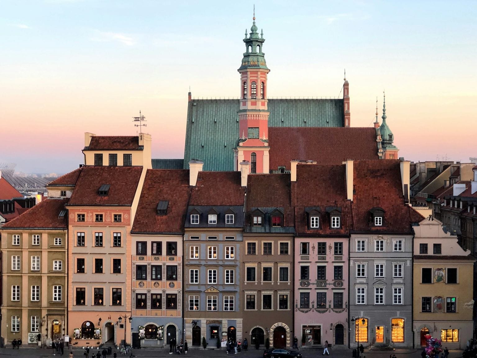 Pastel townhouses of the Old Town Market Square in Warsaw at dusk, with church towers rising behind
