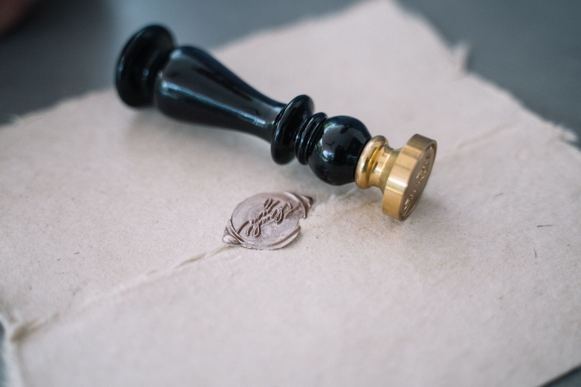 A brass wax seal stamp beside a wax seal pressed onto handmade paper